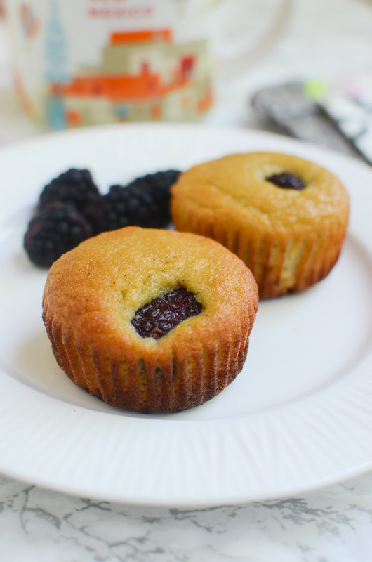 Two paleo blackberry muffins and fresh blackberries on a white plate; coffee mug in the background