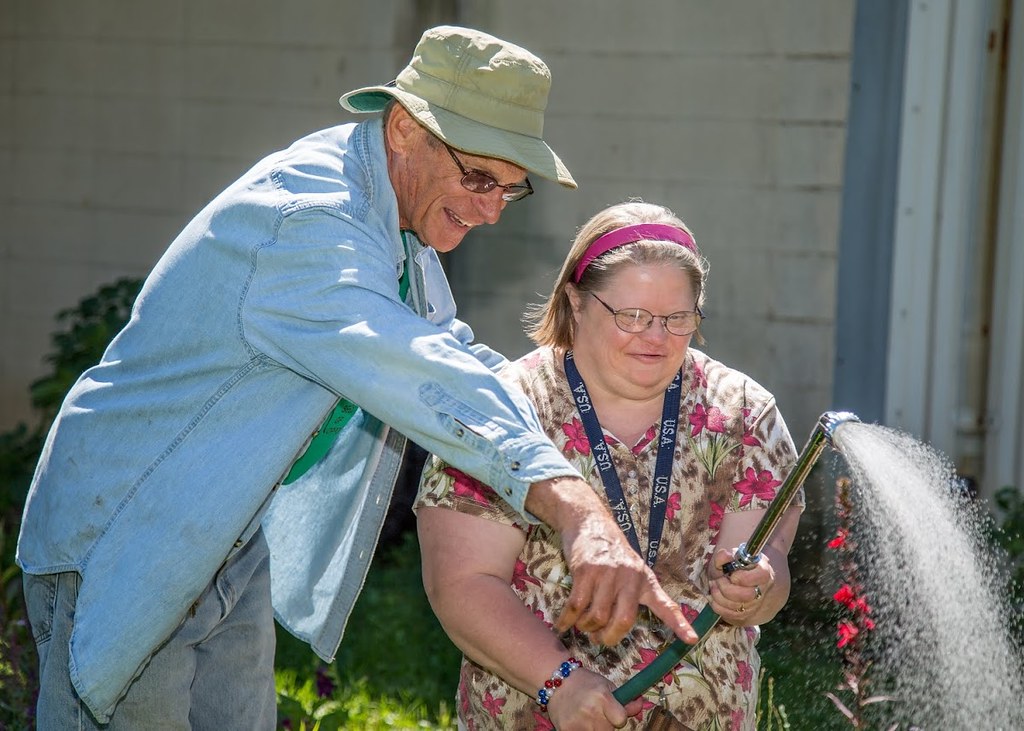 Volunteer helping young woman water plants