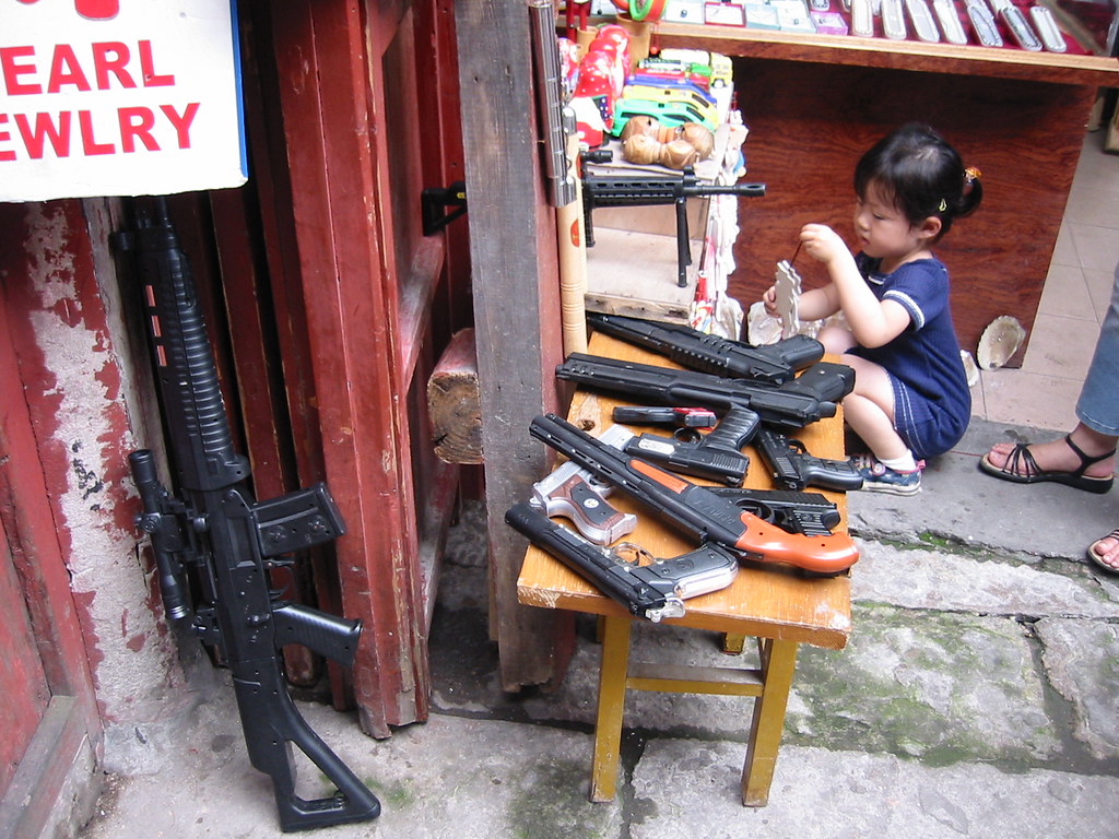 A toy shop selling very realistic looking guns, with tiny child in corner