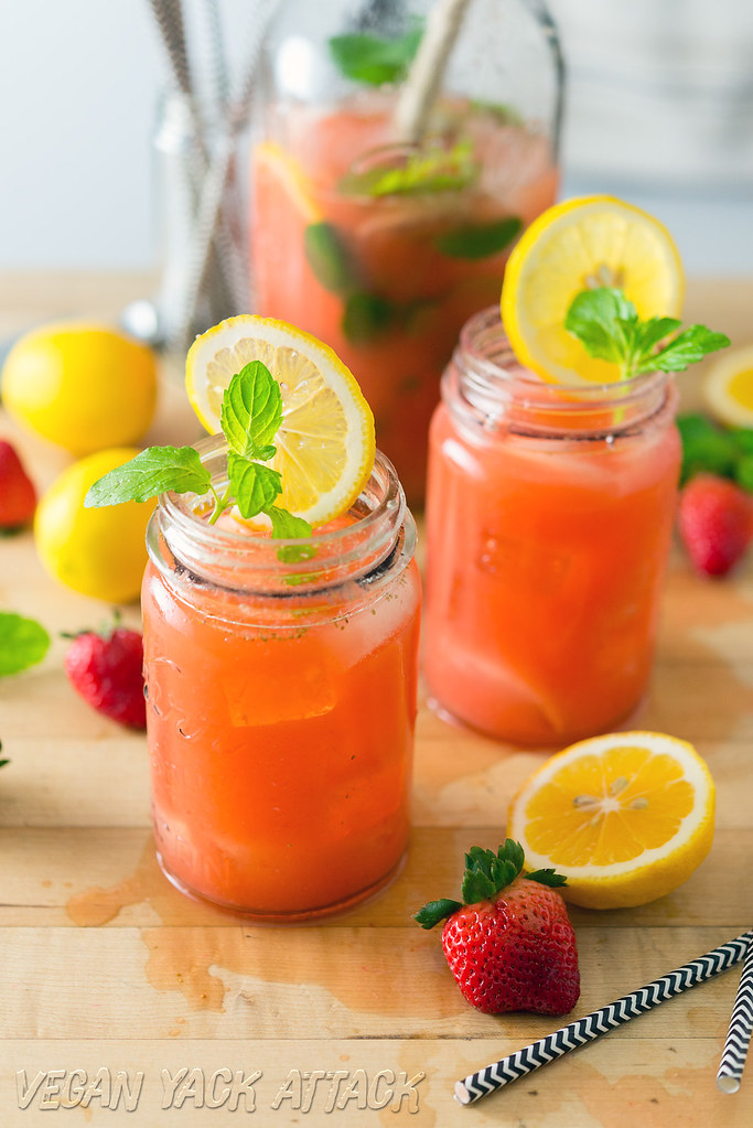 A couple of glasses of boozy mint strawberry lemonade next to a large jar of it