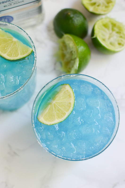 Overhead shot of blue margaritas with squeezed limes next to them