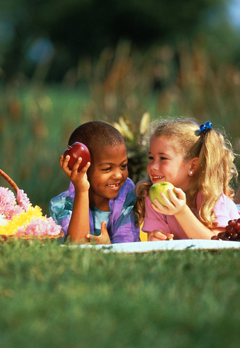 A boy and girl smiling and holding fruits in their hands