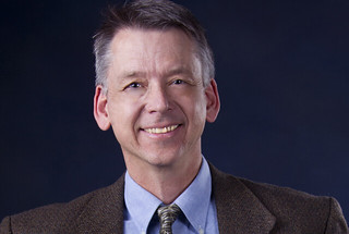 photo of Bruce Carlsten wearing a brown suit jacket and tie with a blue shirt