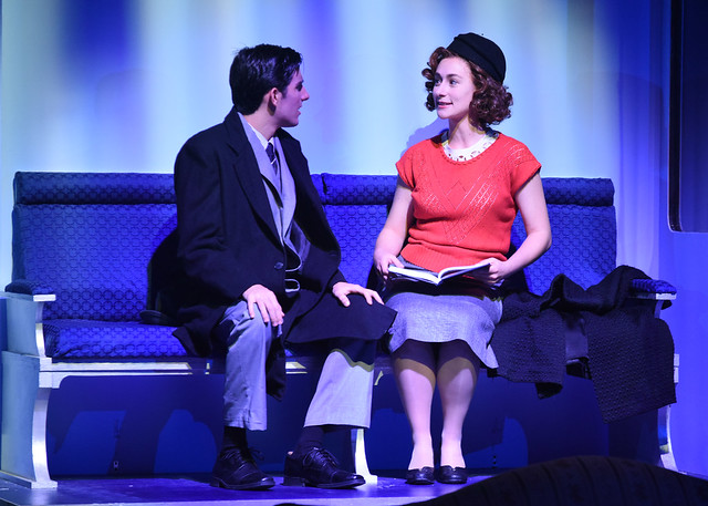 Two people sit on a bench during a theater production