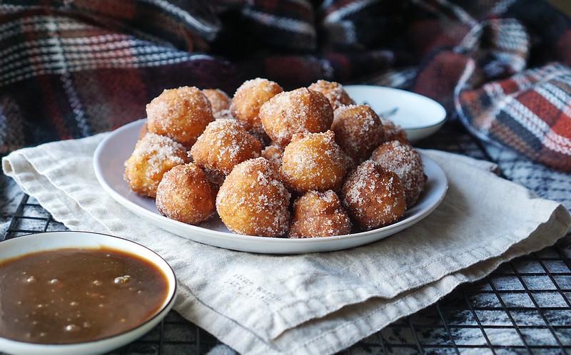 Plate of gluten free churro donut holes rolled in cinnamon sugar with a homemade caramel dipping sauce.