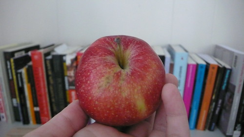 A photo of an apple in a person's hand with books in the background. 