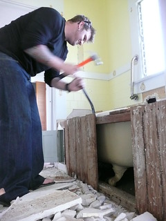 A dude ripping apart a tub surround with a hammer and crowbar (in sandals!).