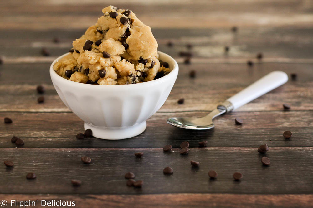 white bowl filled with gluten free cookie dough with chocolate chips on a wooden table sprinkled with mini chocolate chips