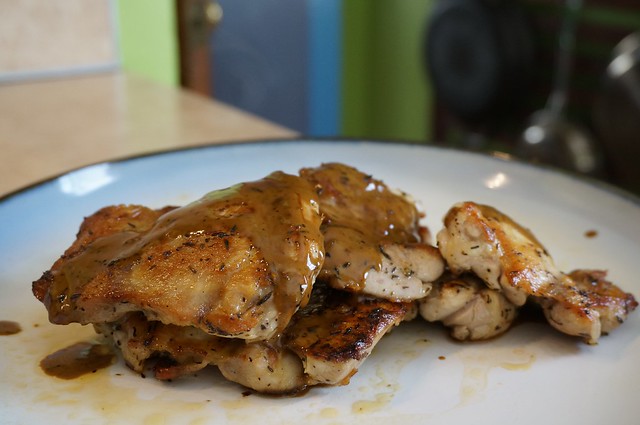 Pan-seared lemony chicken thighs, in closeup on a plate, with a rack of pans blurry in the background