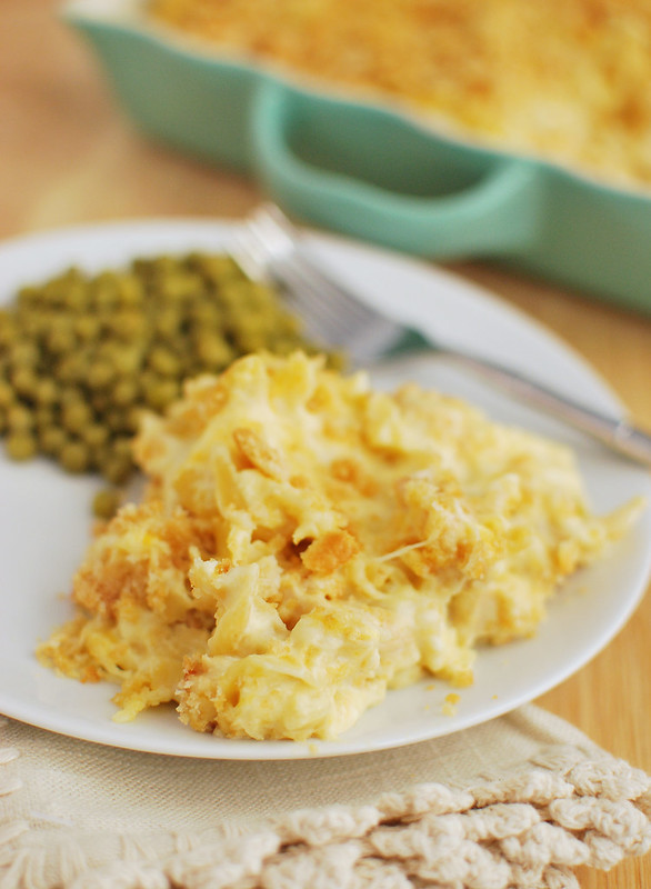 Cheesy chicken noodle casserole on a white plate with peas in the background