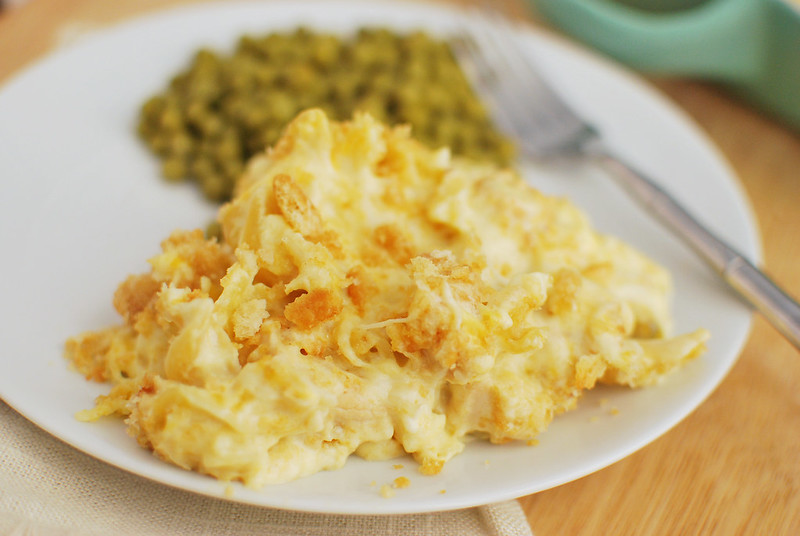 A serving of cheesy chicken noodle casserole on a white plate with peas and a fork. 