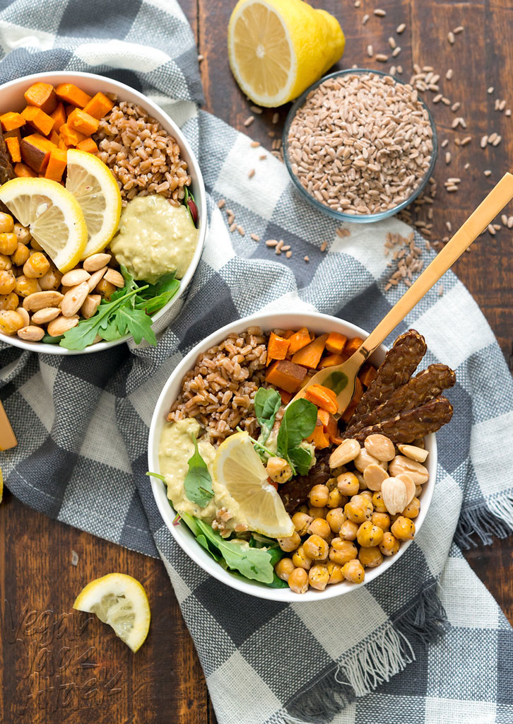 Two vegan fall farro protein bowls filled with almonds, farro, hummus, arugula, roasted chickpeas, tempeh bacon, and sweet potatoes