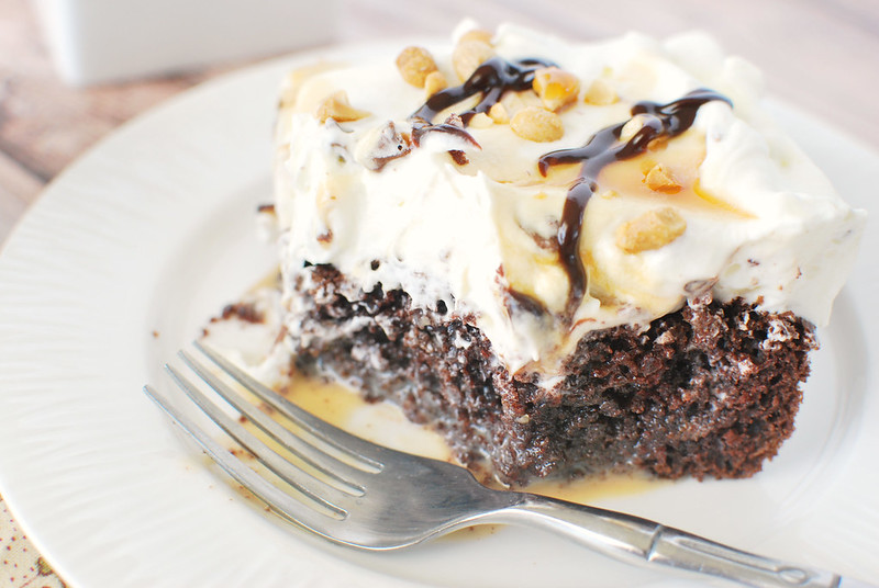 Snickers Cake - chocolate poke cake filled with sweetened condensed milk and caramel. It's topped with whipped cream and chopped Snickers! Plus, peanuts, caramel sauce, and hot fudge on top! 