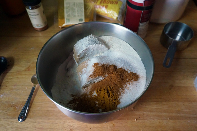 Dry ingredients in a stainless steel mixing bowl, the big rounds of packed brown sugar dusted with cinnamon, flour, and curry powder
