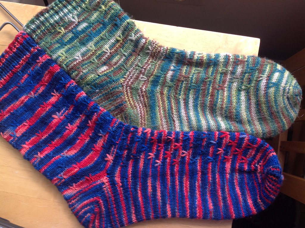 Two handknit socks, same pattern, older one faded, newer one still vibrant.
