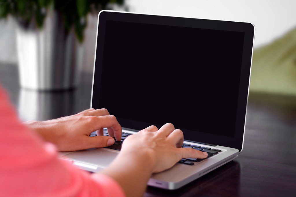 A woman typing on a laptop with a black screen