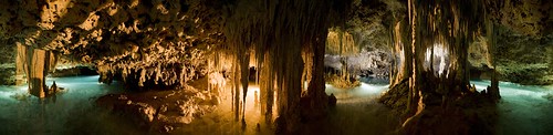 panorama of a cave with blue water on either side and stalactites in an orange hue