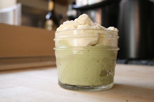 A very close up shot of a 4 oz mason jar filled 4/5 with avocado mousse, then topped with whiped cream that is a tad over whipped.