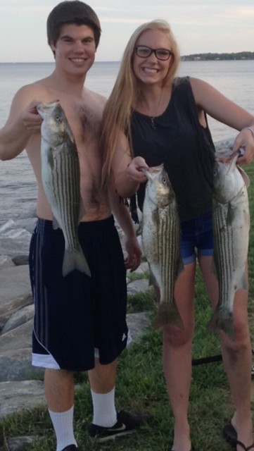 A man and a woman both holding striped bass
