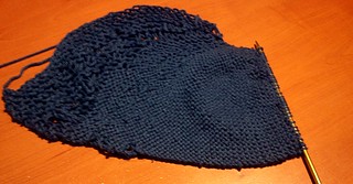 Knitting in dark blue yarn on a desk; the tension is very uneven