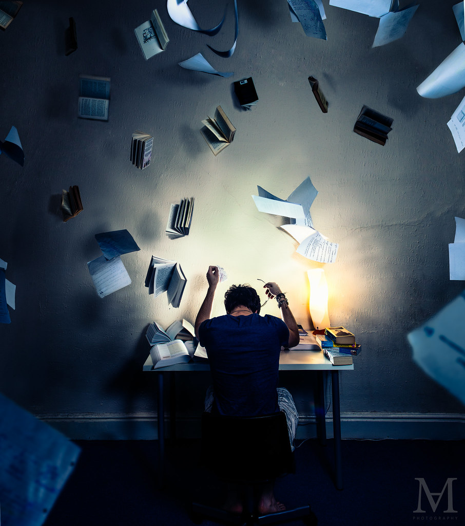 Tired person at desk working with books flying overhead