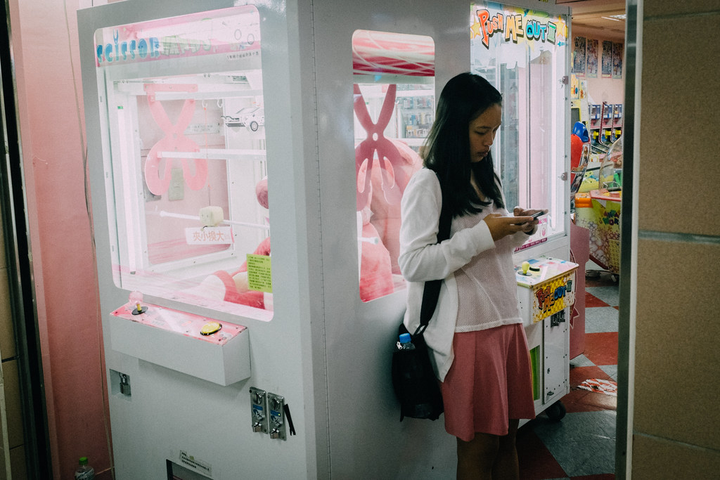Una chica juega con su móvil en la puerta de una sala de recreativas en Taipei City Mall
