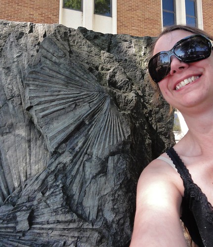 Image is a selfie of me in sunglasses next to a gray rock with fossil palm leaves pressed into it.