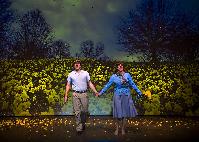 A man and woman hold hands as they walk through a field of daffodils during a production of Big Fish.