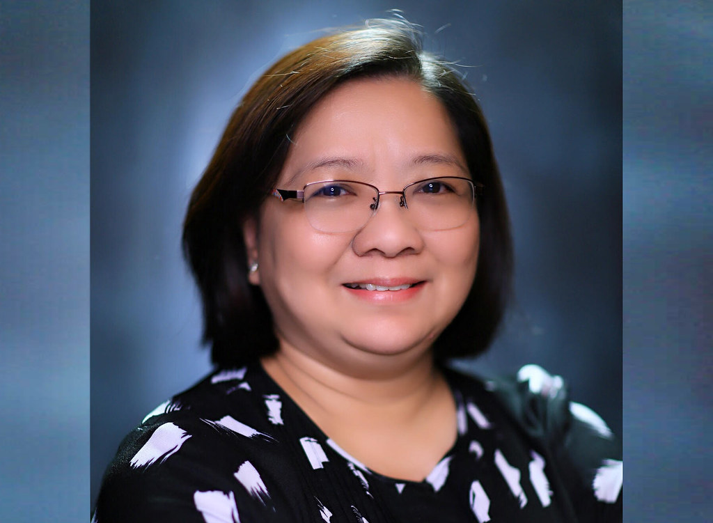 The image shows Dr. Ermenilda Avendaño smiling and wearing black shirt with white spot designs and eyeglasses.