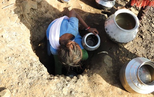 मध्य प्रदेश के उमरिया जिले के बाजाकुंड गाँव में खाई से पानी निकालती महिला